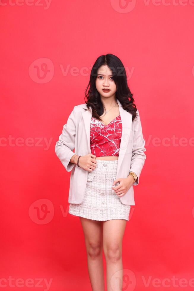 Portrait of an elegant young Asian Indonesian woman wearing a cream-colored blazer. Isolated red background for content materials, banners, advertising. photo