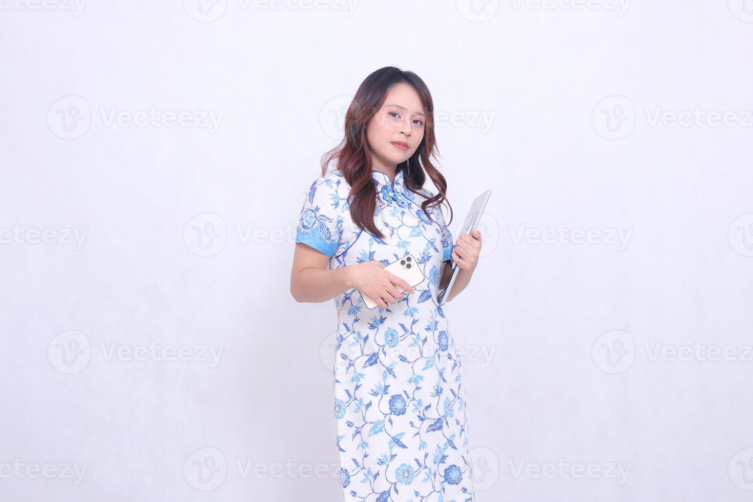 Beautiful Indonesian Chinese woman wearing modern Chinese blue dress holding tablet and cellphone isolated on white background photo