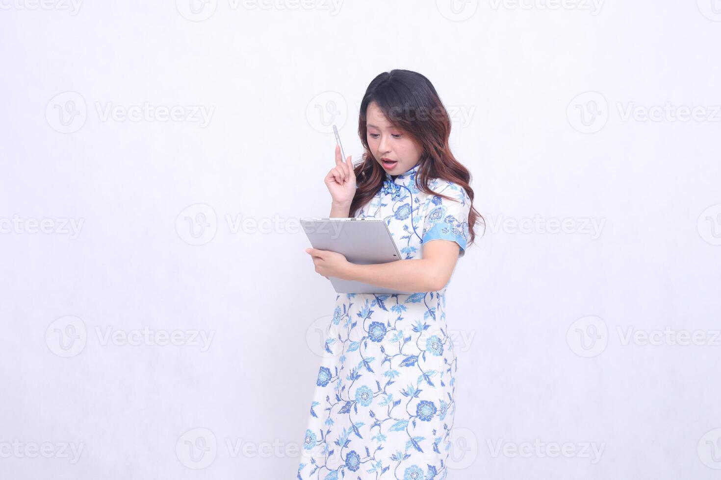 Beautiful shocked Indonesian Chinese woman wearing modern Chinese blue dress carrying tablet and looking at it isolated white background photo