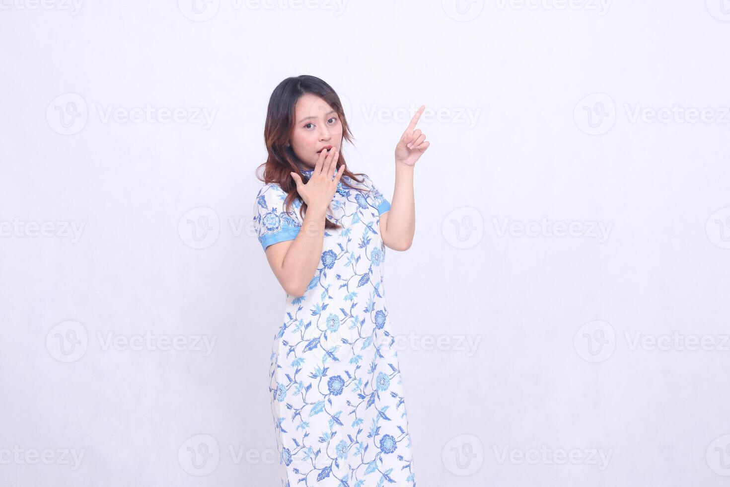 Beautiful shocked Javanese Chinese woman wearing a modern Chinese dress, front view and hand pointing to the top left on a white background. happy Chinese New Year photo
