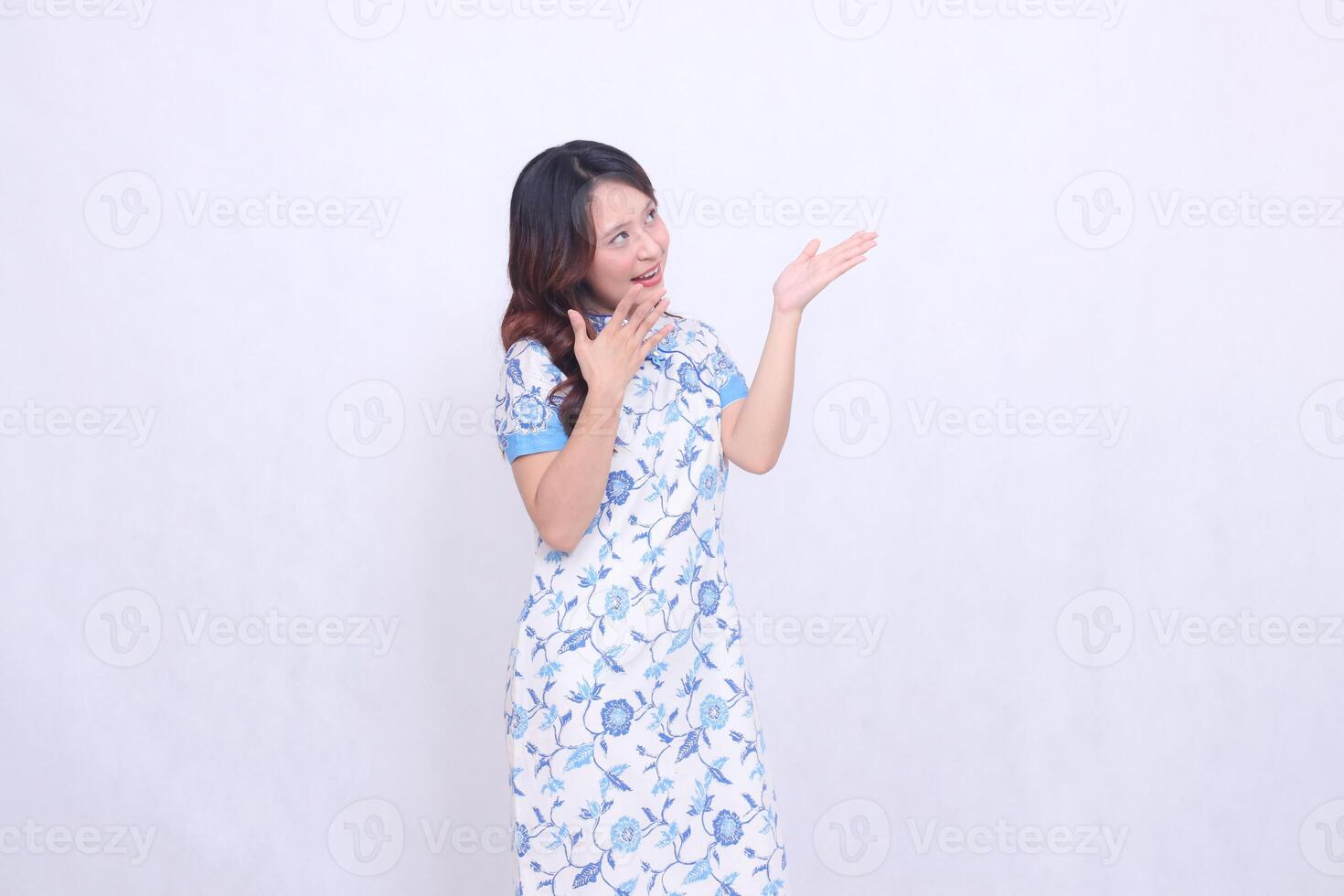Beautiful cheerful Javanese Chinese woman wearing modern Chinese dress view top left and hand presenting isolated white background. happy Chinese New Year photo