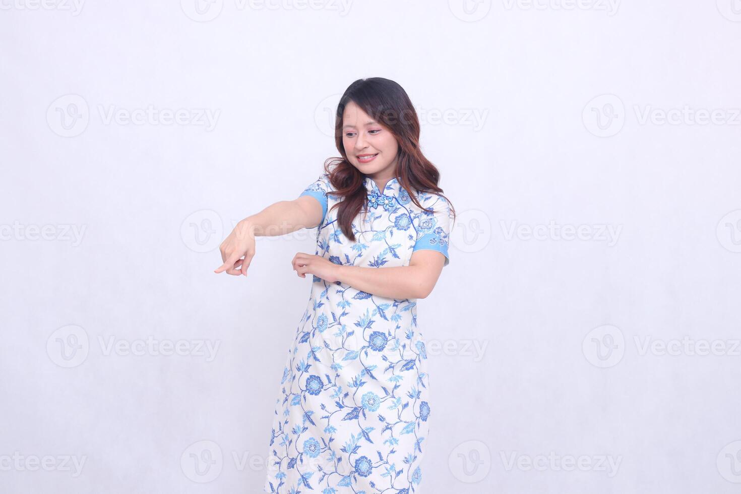 Beautiful Chinese Javanese woman smiling wearing a modern Chinese dress with her arms crossed pointing to the bottom left on a white background. happy Chinese New Year photo