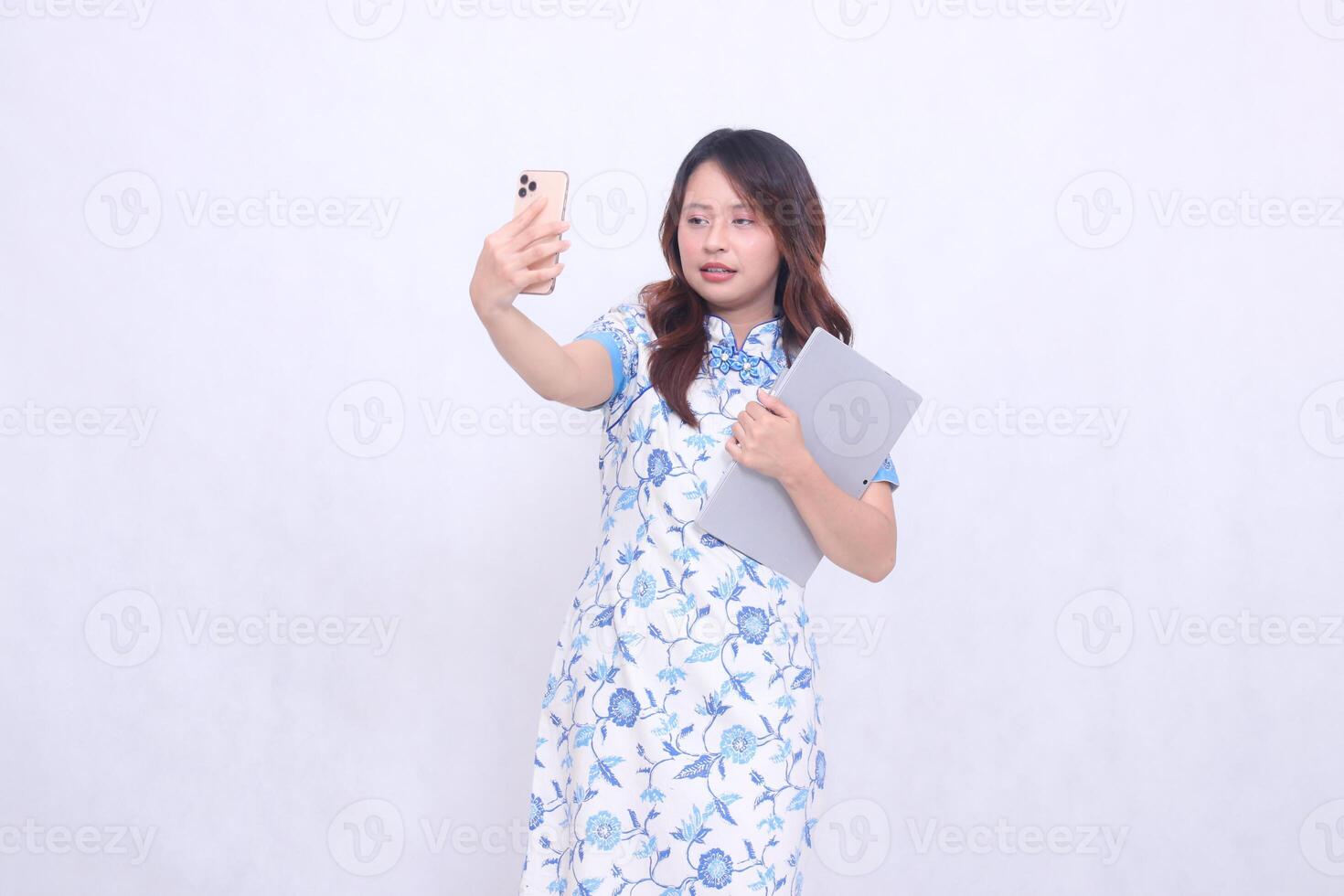 beautiful asian woman wearing modern chinese blue dress obliquely sleepy holding tablet and looking at cell phone up isolated white background photo