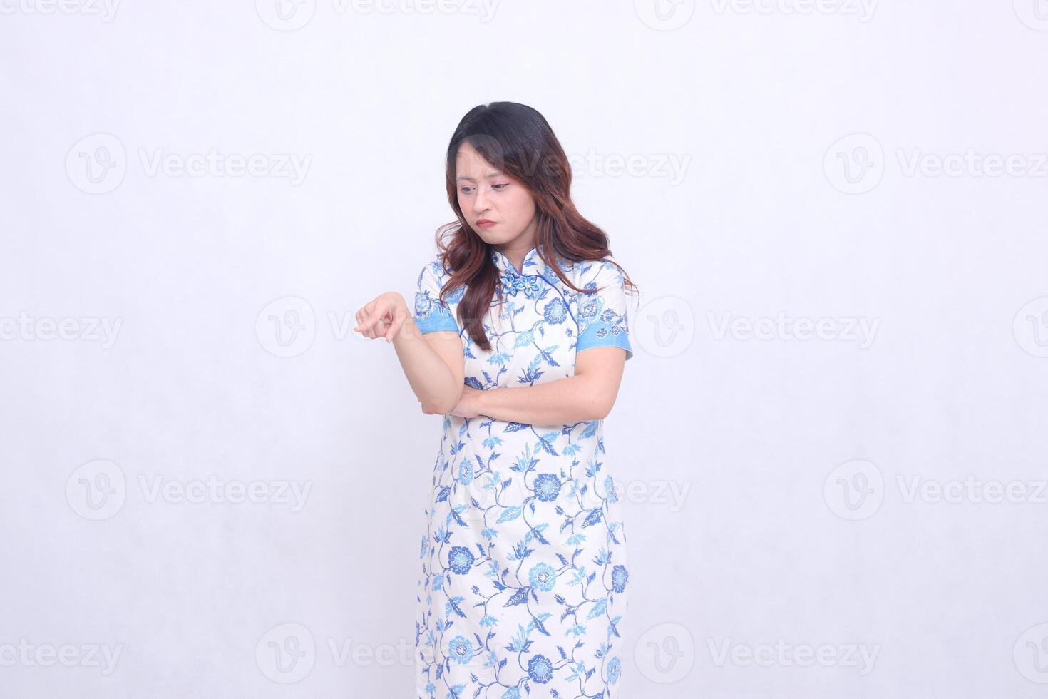 Beautiful Javanese Chinese girl pouting wearing a modern Chinese dress with her arms crossed pointing to the bottom left on a white background. happy Chinese New Year photo