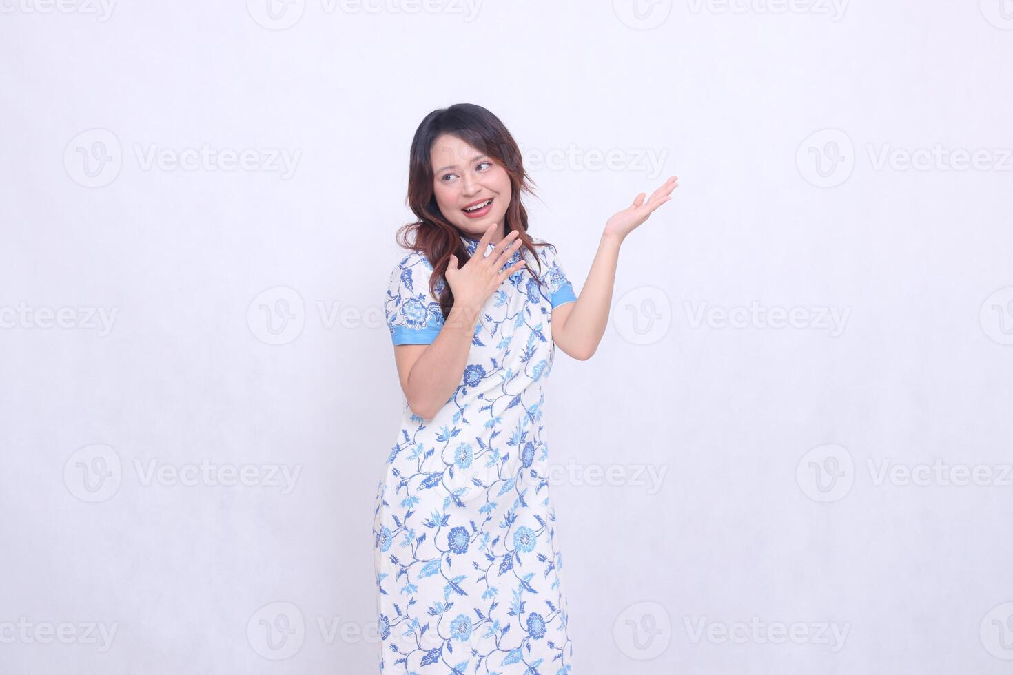Beautiful cheerful Javanese Chinese girl wearing modern Chinese dress looking left and hand presenting isolated white background. happy Chinese New Year photo