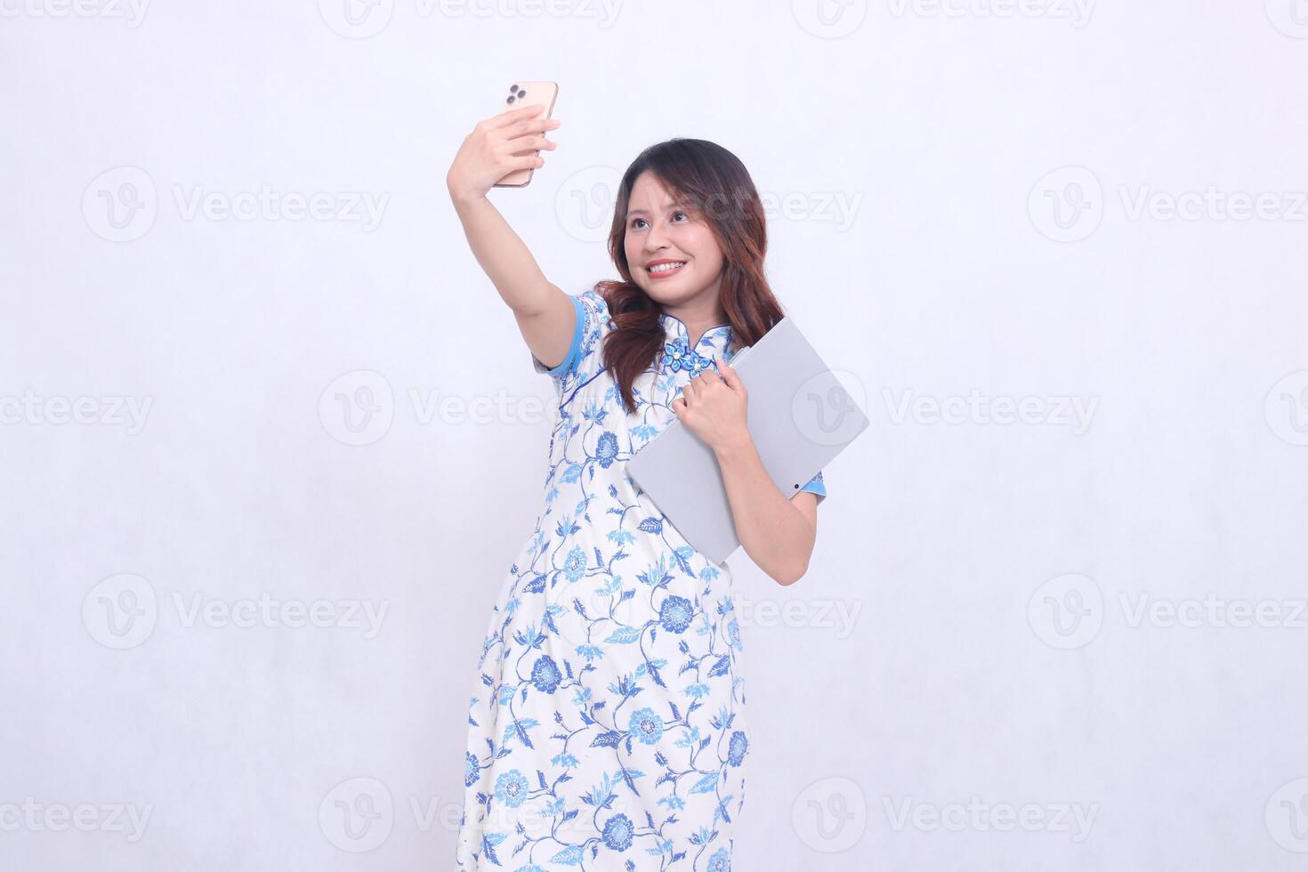 beautiful asian woman wearing modern chinese blue dress obliquely cheerful holding tablet and looking at cell phone up isolated white background photo