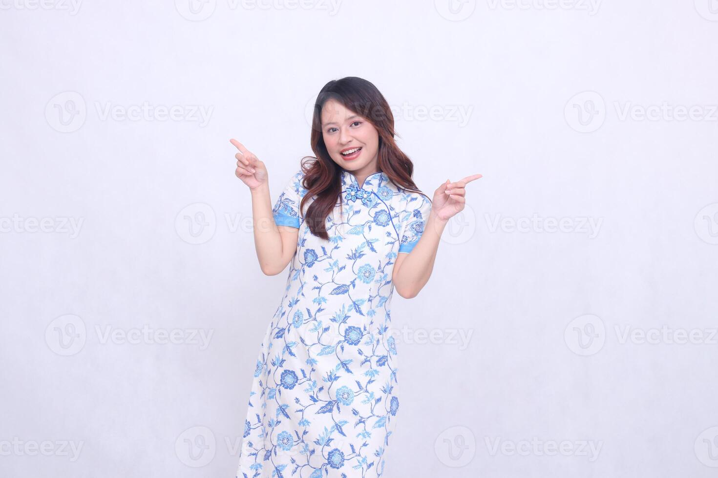 beautiful cheerful chinese woman wearing modern chinese dress hands all pointing up tilted left right on white background. happy Chinese New Year photo