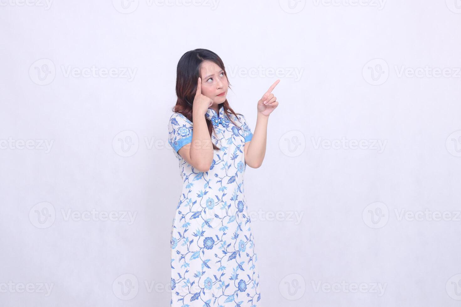 beautiful Javanese Chinese woman thinking wearing a modern Chinese dress showing her brain and hand pointing up left on a white background. happy Chinese New Year photo