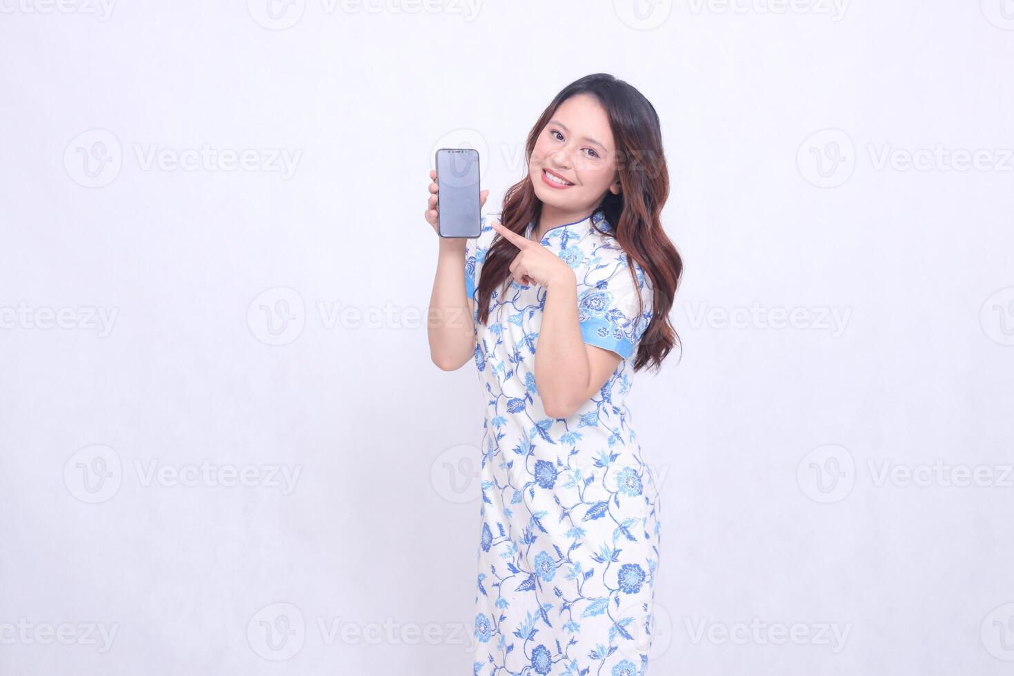 young asian javanese chinese girl wearing traditional chinese blue dress happy promoting and pointing gadget on cellphone screen isolated white background photo