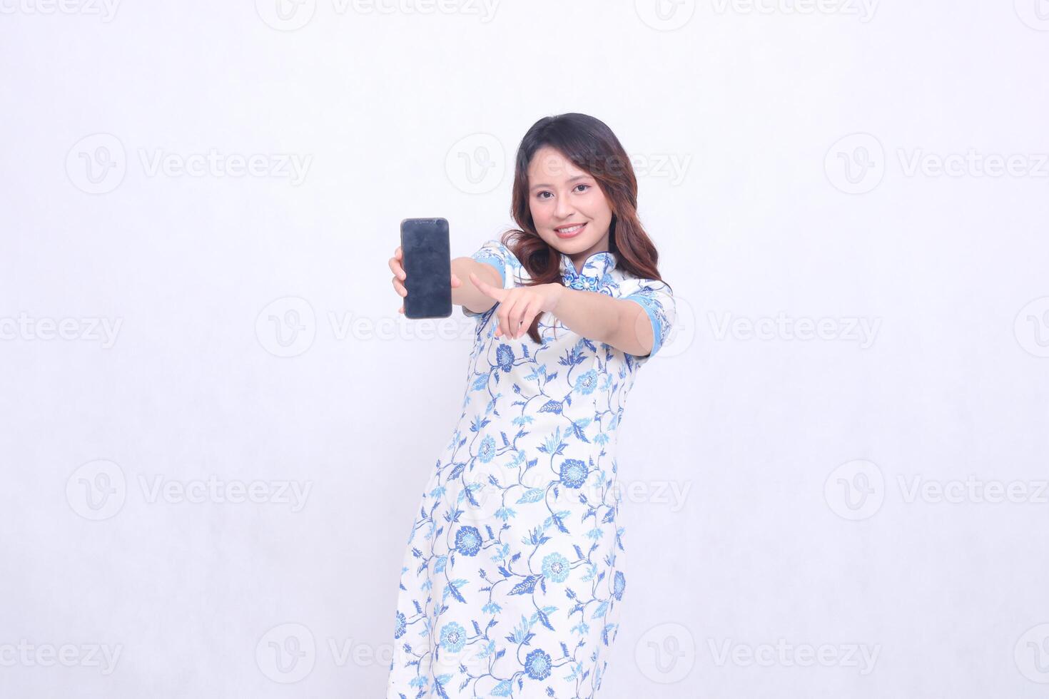 young Indonesian Javanese woman wearing blue traditional Chinese dress happy with arms wide holding gadget showing cellphone screen forward pointing isolated white background photo