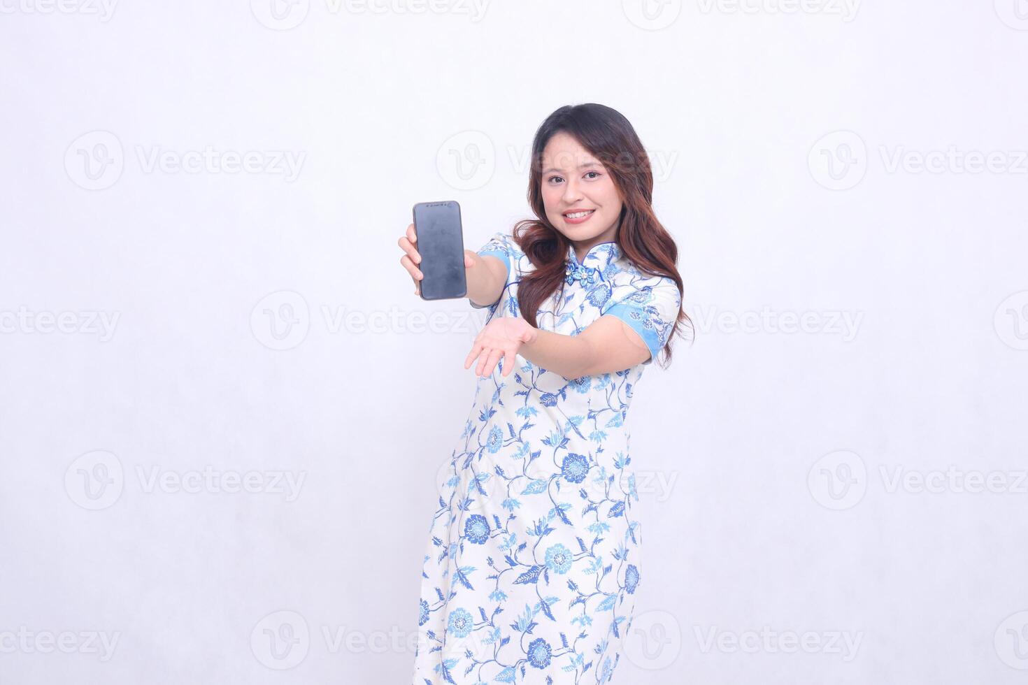 young Indonesian Javanese girl wearing a blue traditional Chinese dress cheerfully holding a gadget showing her cellphone screen raised to the front isolated on a white background photo