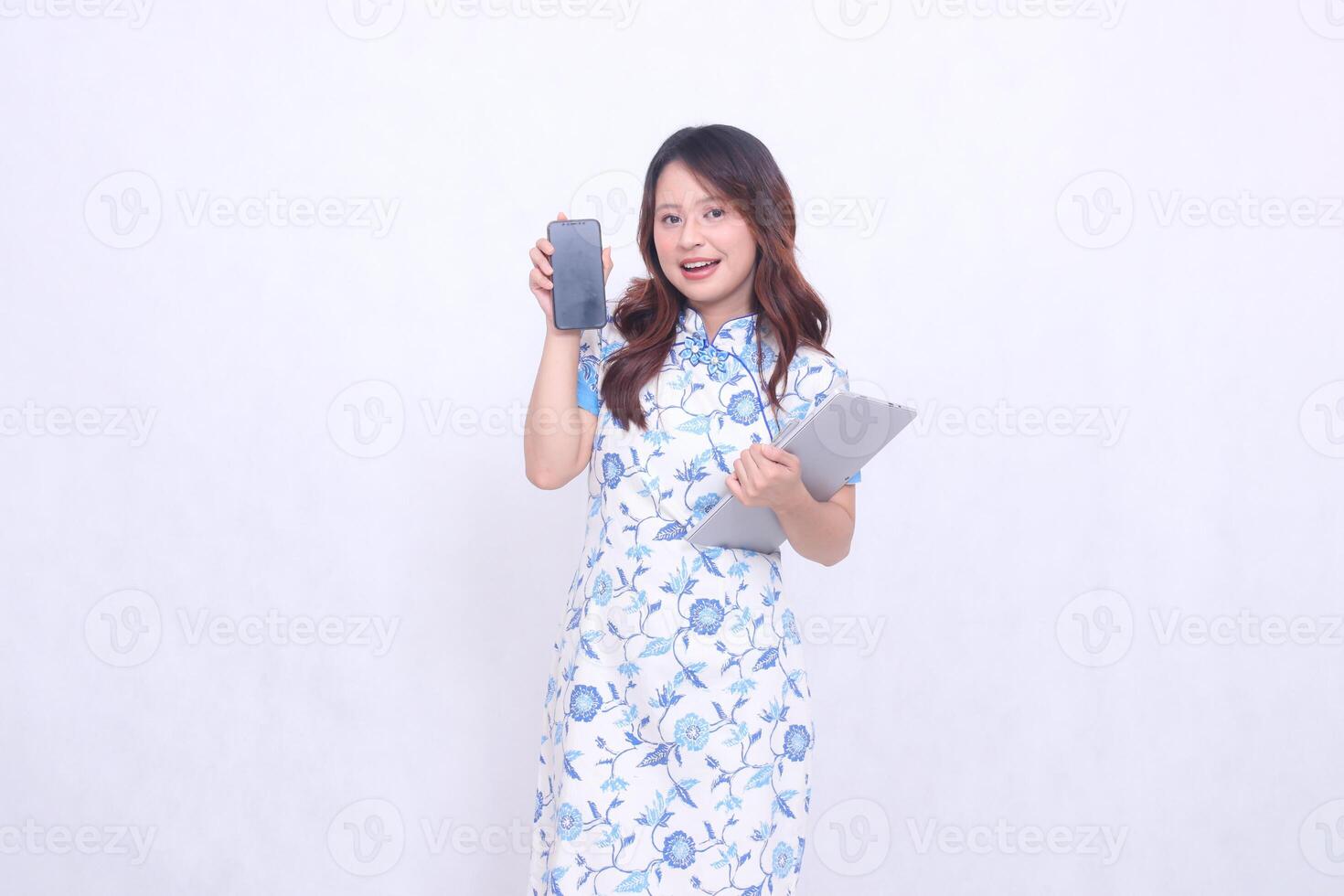 beautiful asian woman wearing blue chinese dress happy holding tablet and looking at cell phone screen isolated white background photo