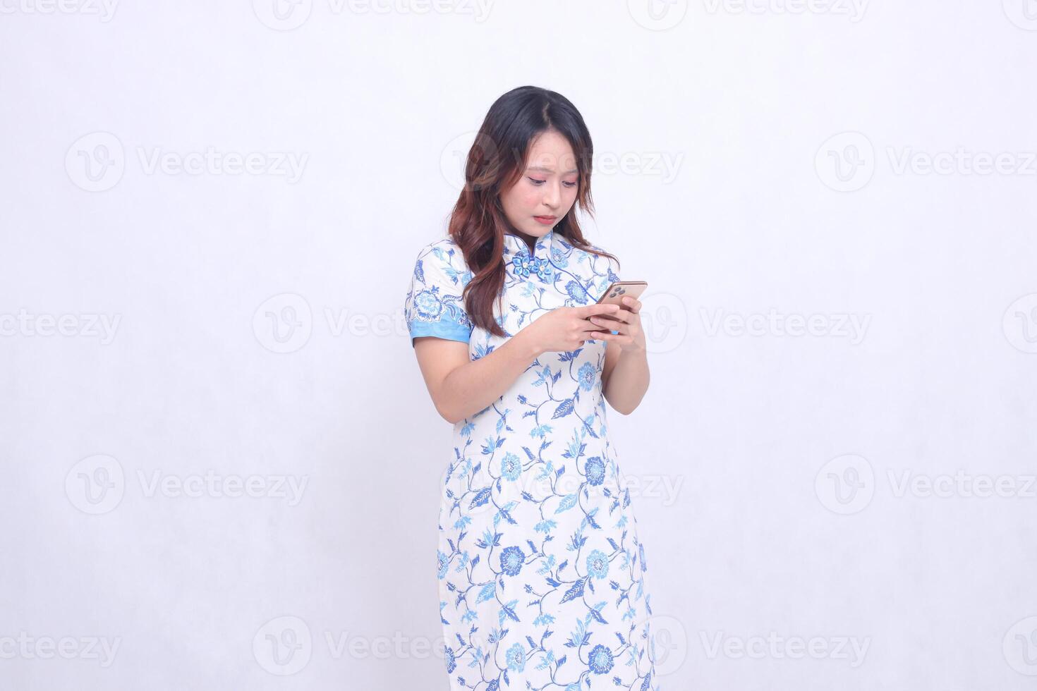 Young Asian Javanese Chinese woman wearing a left-slanted Chinese blue dress while focusing on typing on a gadget isolated on a white background photo