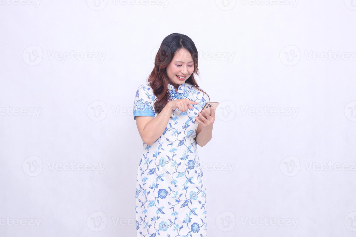 young Asian Javanese Chinese woman smiling laughing wearing blue Chinese dress tilted left while operating gadget forefinger pressing cell phone isolated white background photo