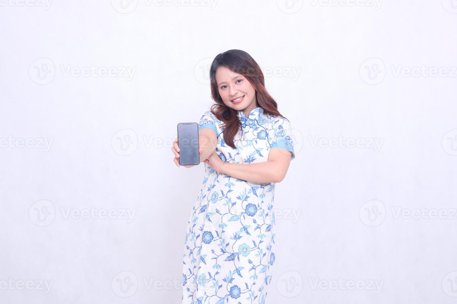 young Indonesian Javanese woman wearing a blue traditional Chinese dress cheerful with her arms wide holding a gadget showing her cell phone screen in front of her isolated on a white background photo