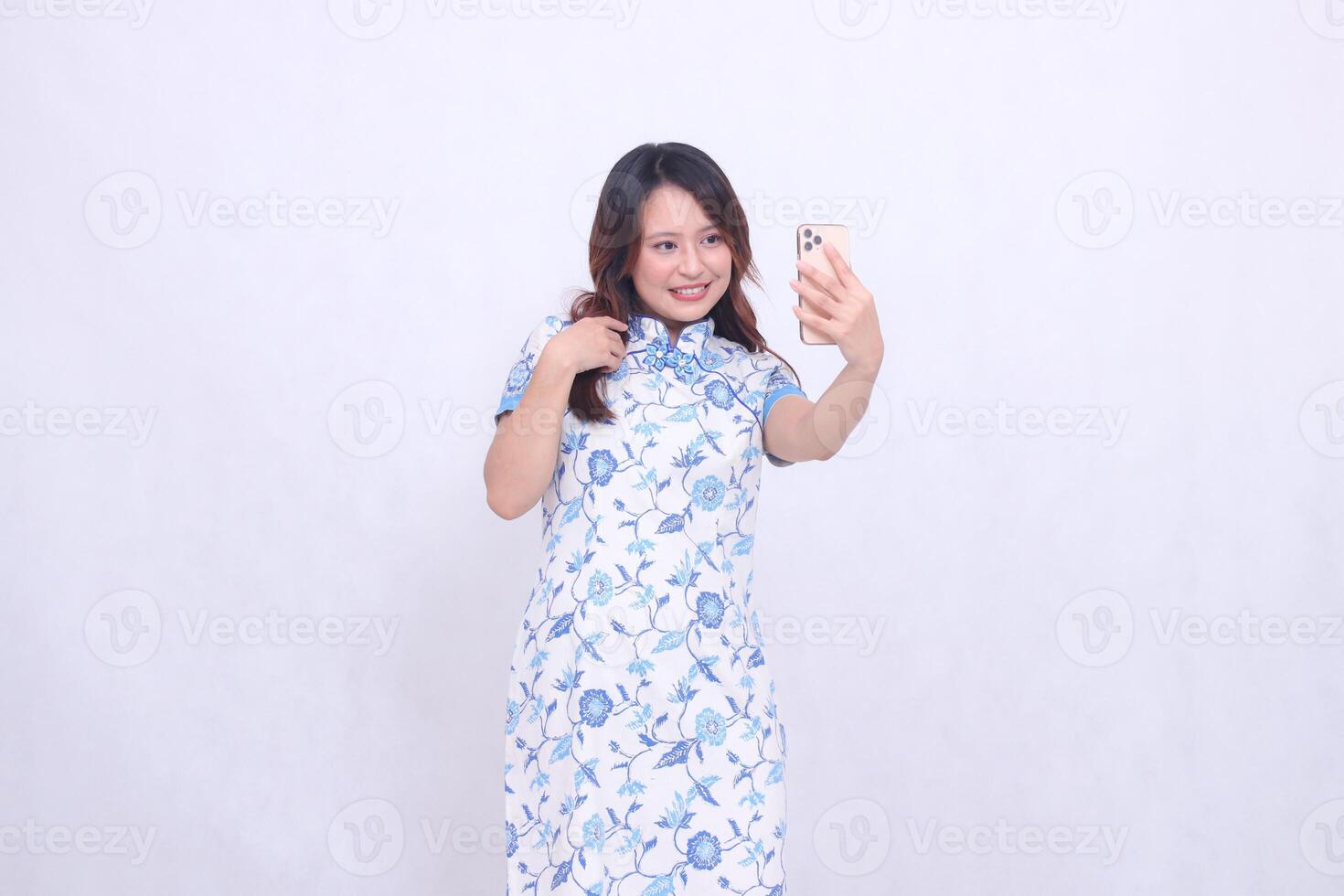 Young Asian Javanese Chinese woman smiles wearing a blue Chinese dress with a left slant while operating a glass gadget isolated on a white background photo