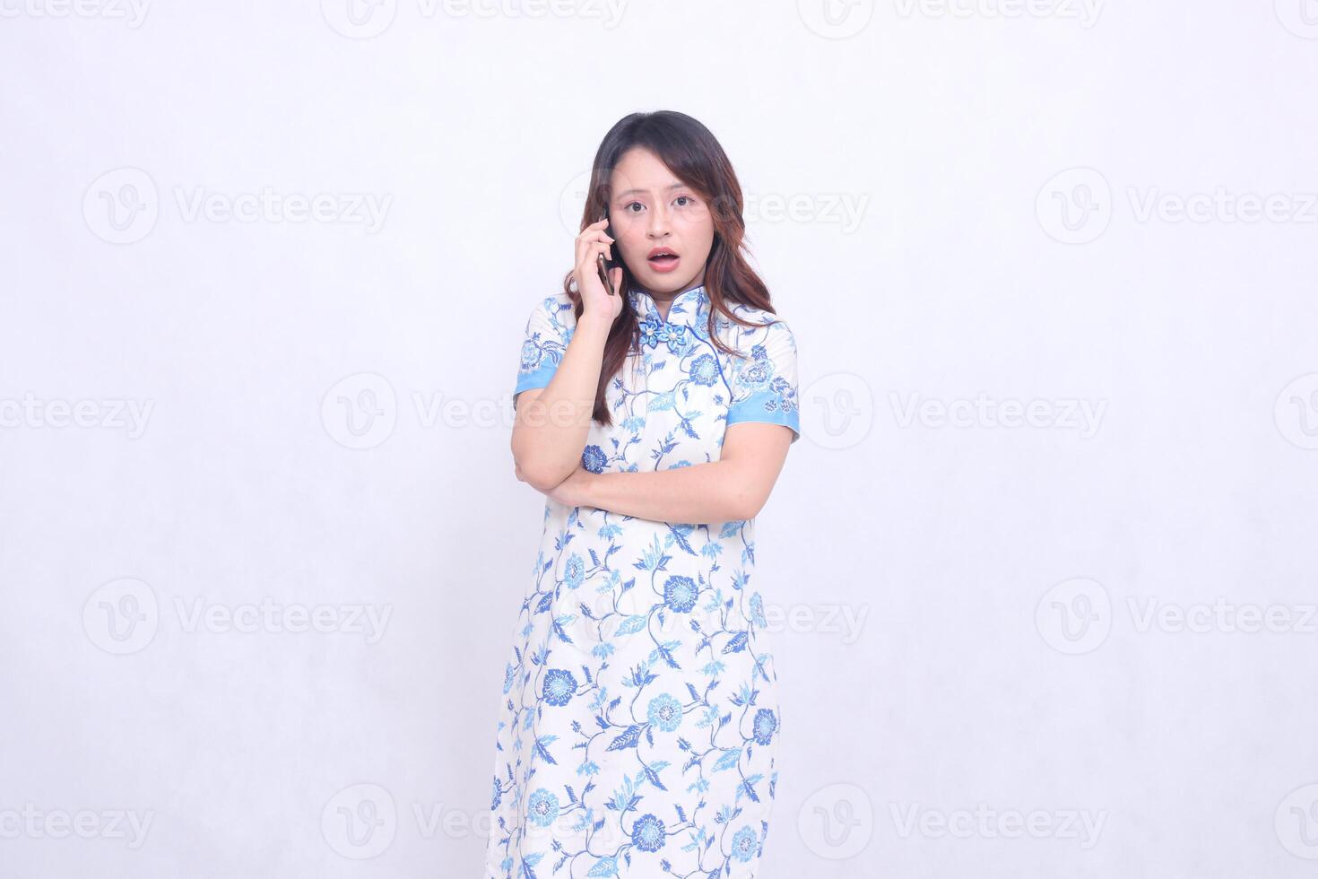 young asian javanese chinese woman very shocked wearing blue chinese dress while on the phone looking at the camera isolated white background photo