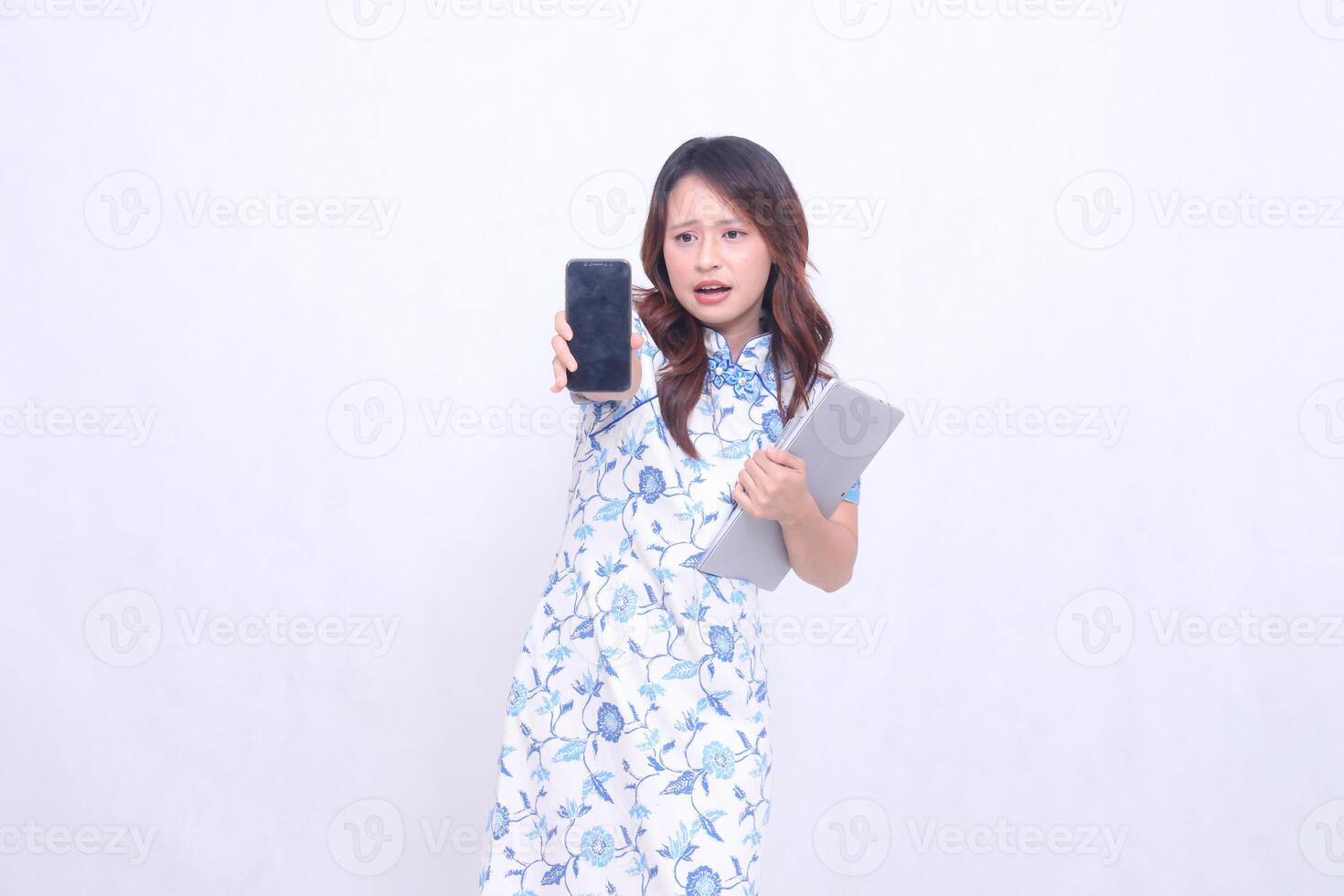 beautiful asian woman wearing blue chinese dress front view thin smile holding tablet and looking at cellphone screen straight up isolated white background photo