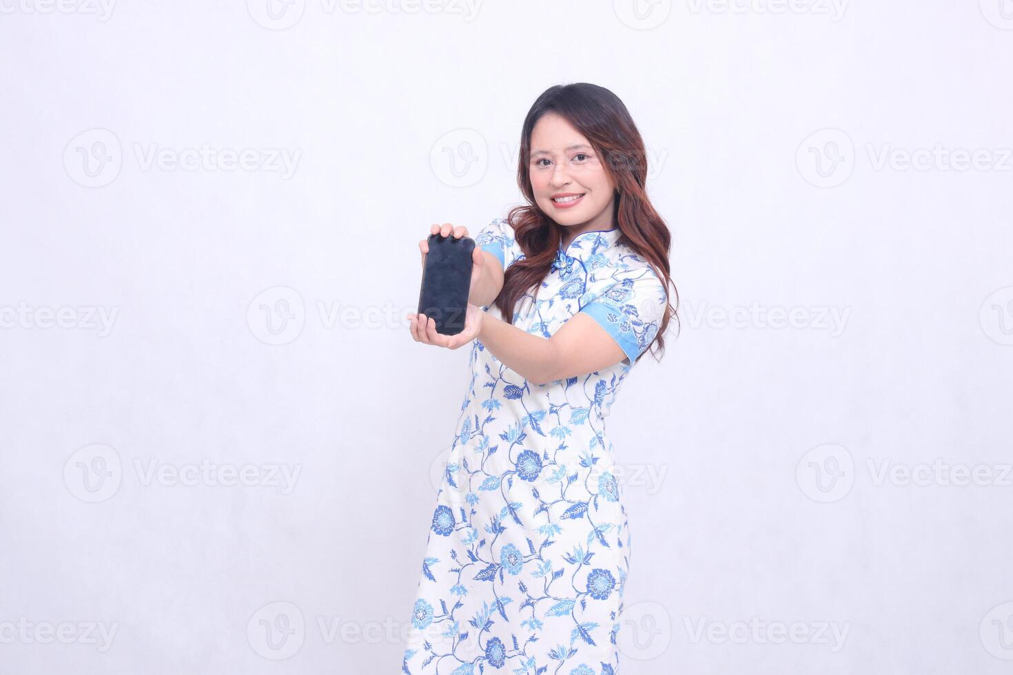 young asian javanese chinese girl wearing chinese traditional blue dress cheerful promoting and holding gadget on mobile phone screen fore isolated white background photo