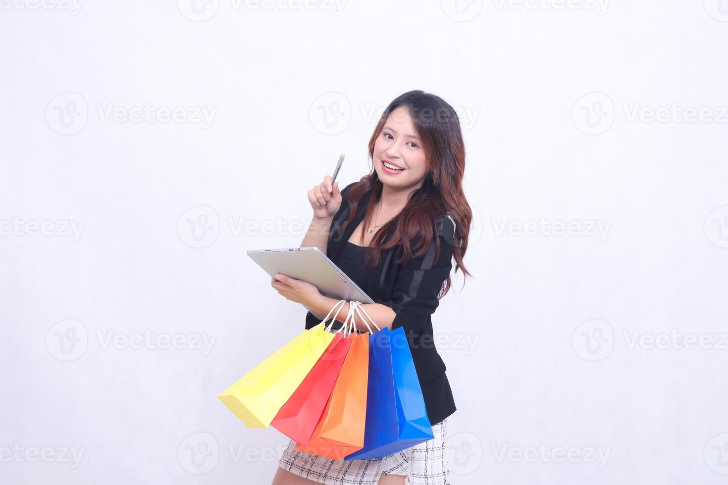 young beautiful woman customer 20s formal office smile laughing in front of tablet pointing in front carrying tablet and paper bag shopping isolated white background photo
