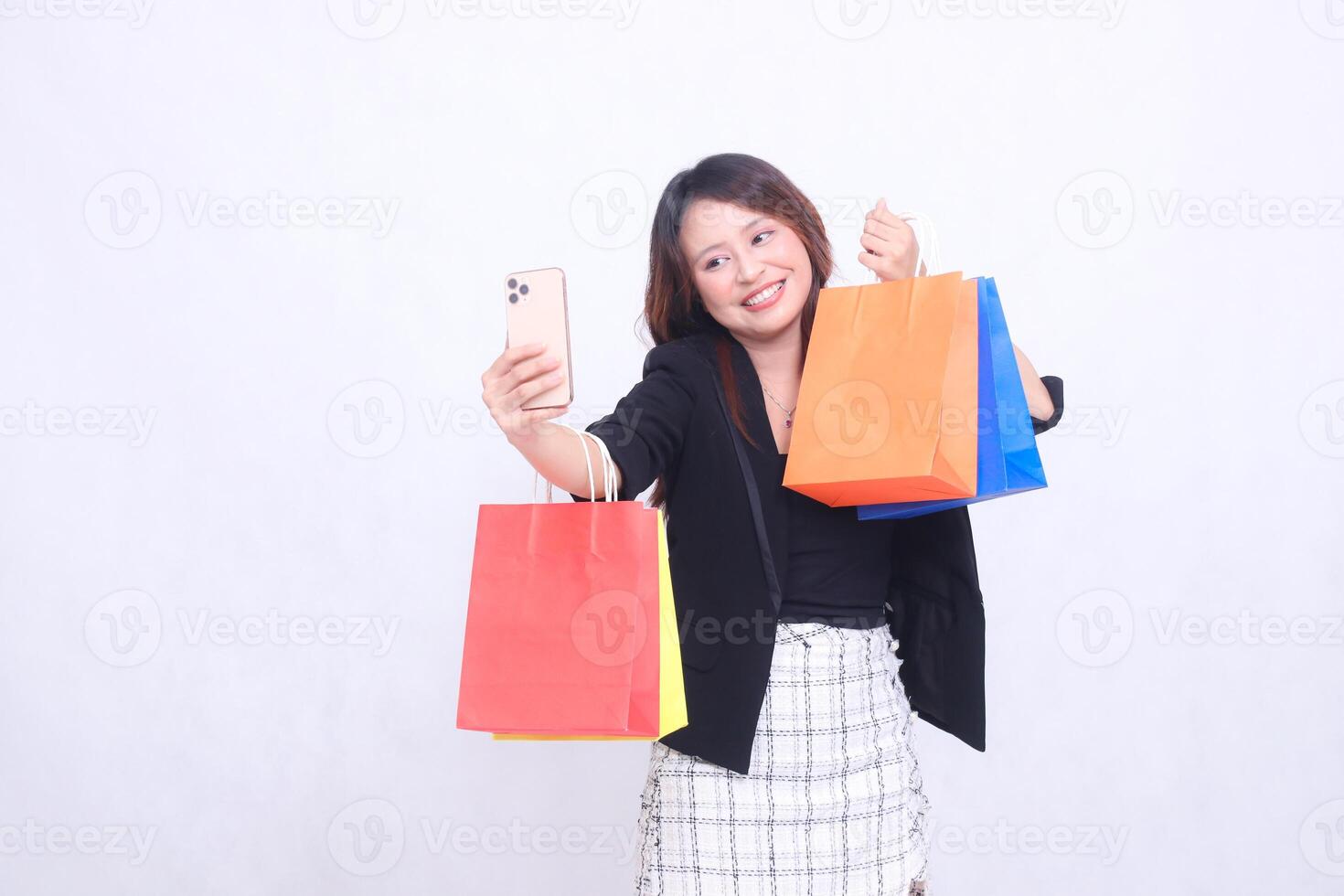 Young beautiful female customer 20s formal office smiling happily while videoing in front of cell phone showing off shopping paper bag isolated on white background photo