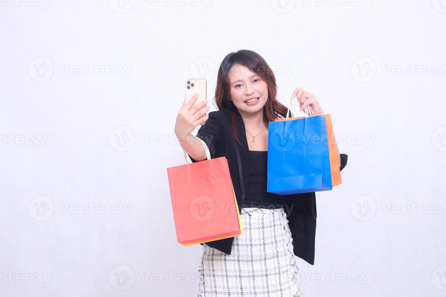 Young beautiful female customer 20s formal office smiling happily while taking photo in front of cellphone looking ahead carrying shopping paper bag isolated on white background