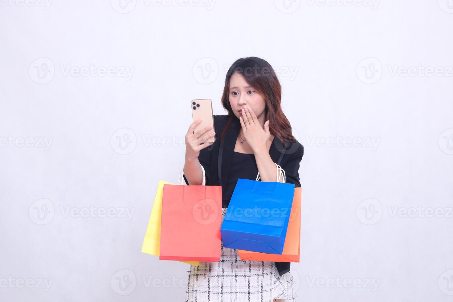 Beautiful Asian girl 20s formal office customer in shock looking at cellphone covering mouth while carrying shopping paper bag isolated on white background photo