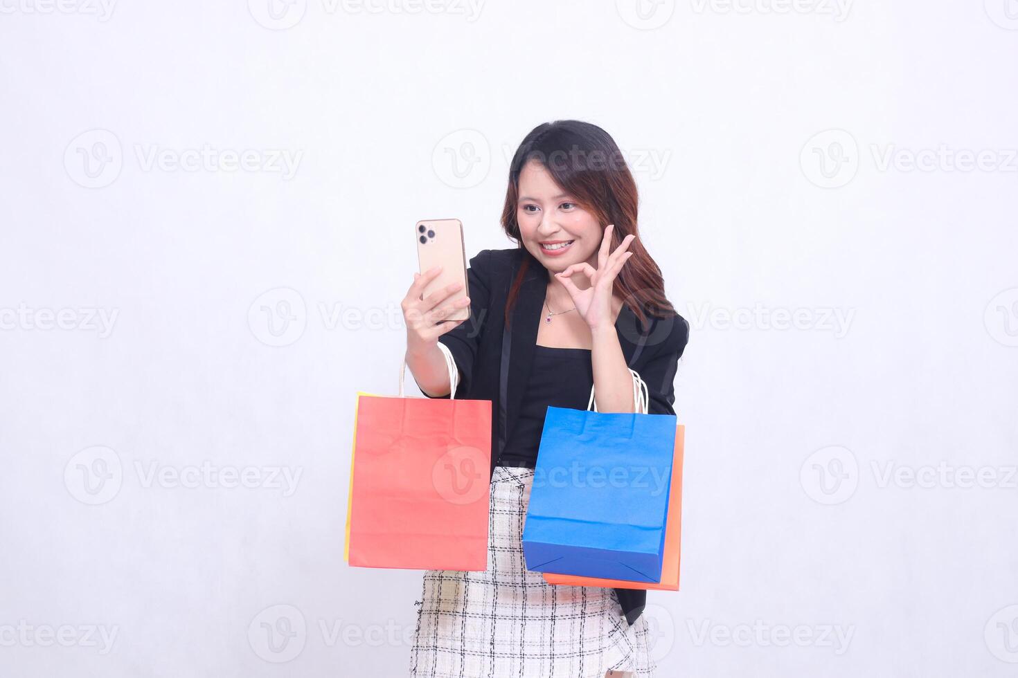 beautiful asian woman customer 20s formal office cheerful smile looking at cell phone hand gesture okay while carrying shopping paper bag isolated white background photo