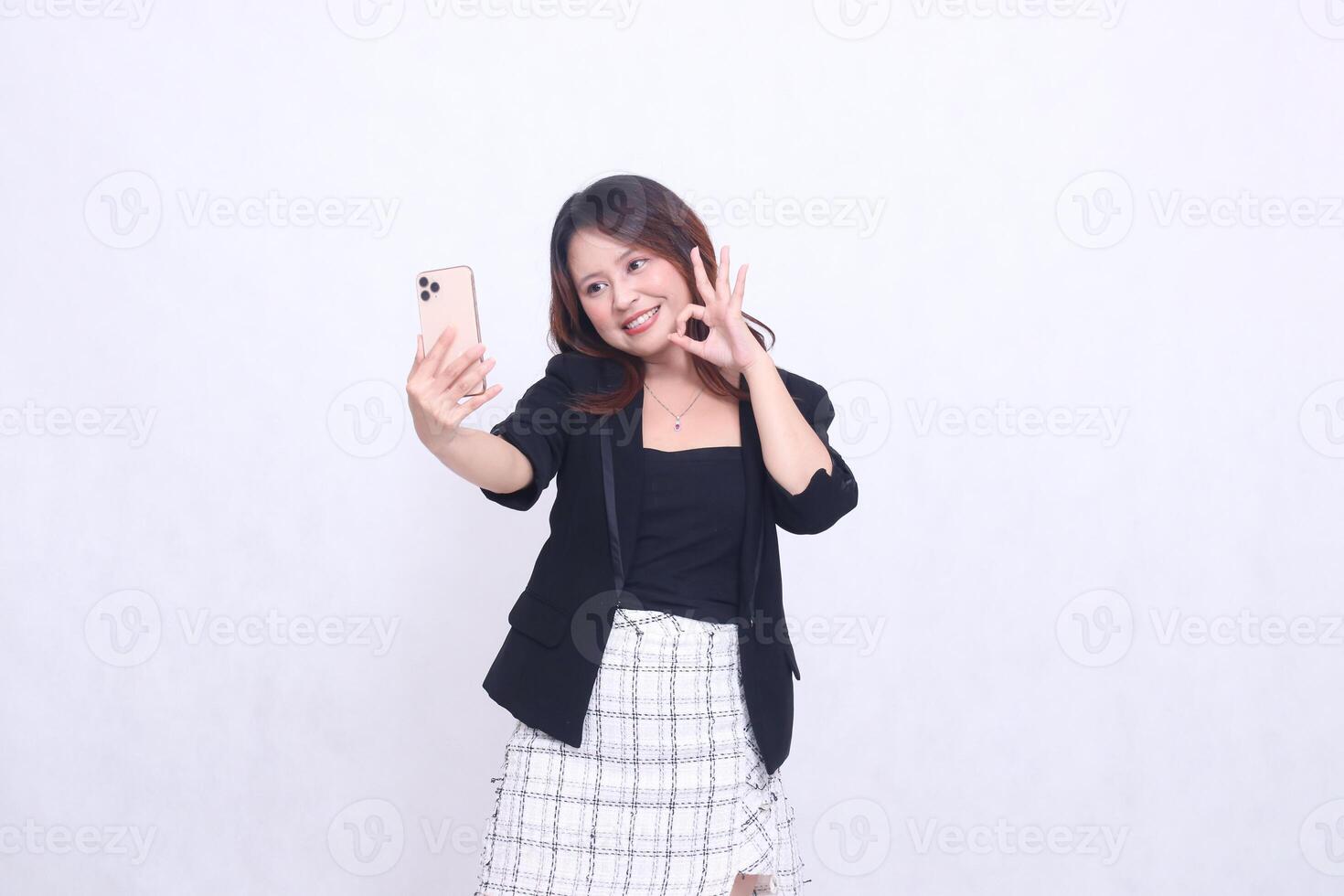 beautiful Indonesian office girl in her 20s, cheerful expression okay, looking at her cream colored cellphone gadget while making a call for a promo isolated on a white background photo
