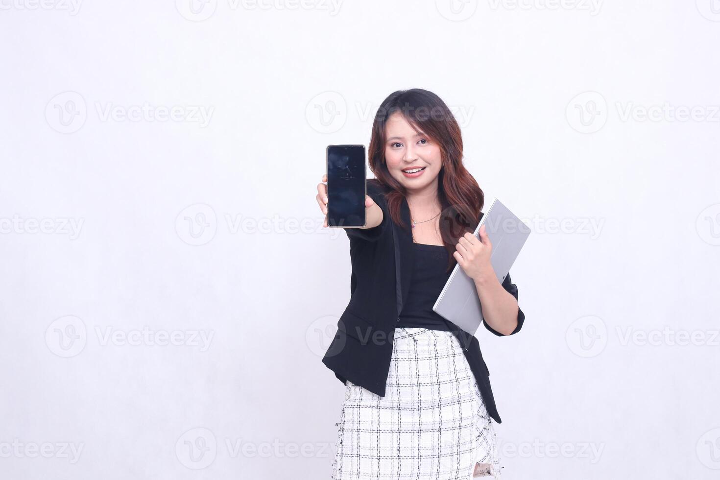 Beautiful Indonesian woman in her 20s, formal office, smiling, looking at a black cellphone gadget and carrying a tablet for promotion, isolated on a white background photo