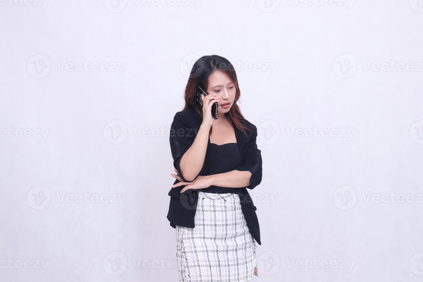 the charm of a beautiful Asian office woman in her 20s, expression chatting on a cellphone gadget with her arms crossed, isolated on a white background photo