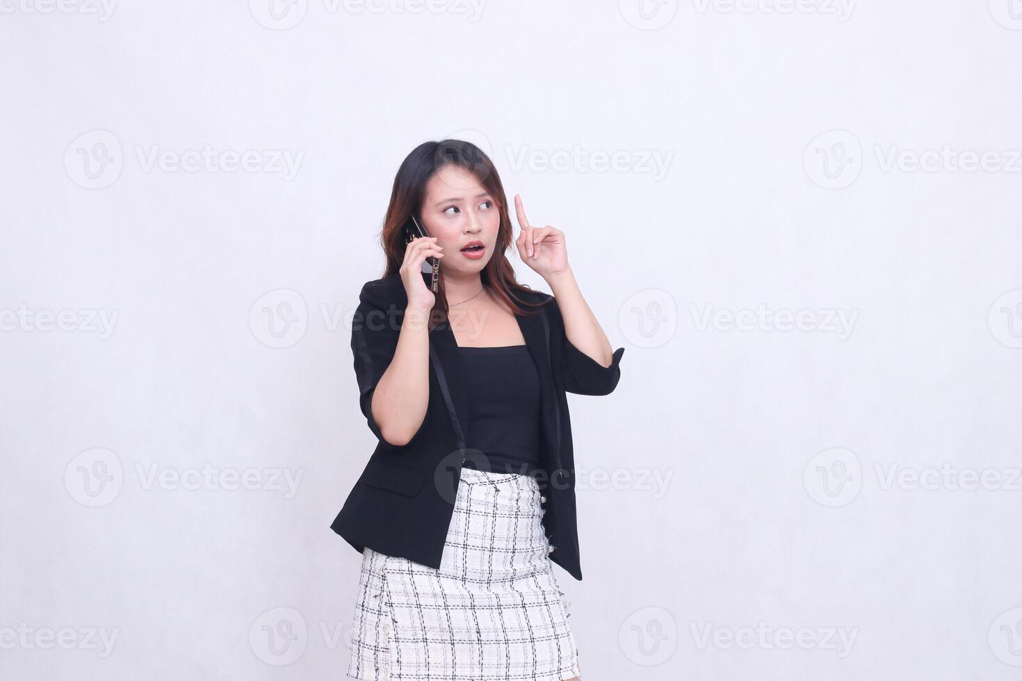 el encanto de un hermosa asiático oficina mujer en su 20s con un sorprendido expresión mientras haciendo un teléfono llamada en un Teléfono móvil artilugio mientras señalando su mano arriba aislado en un blanco antecedentes foto