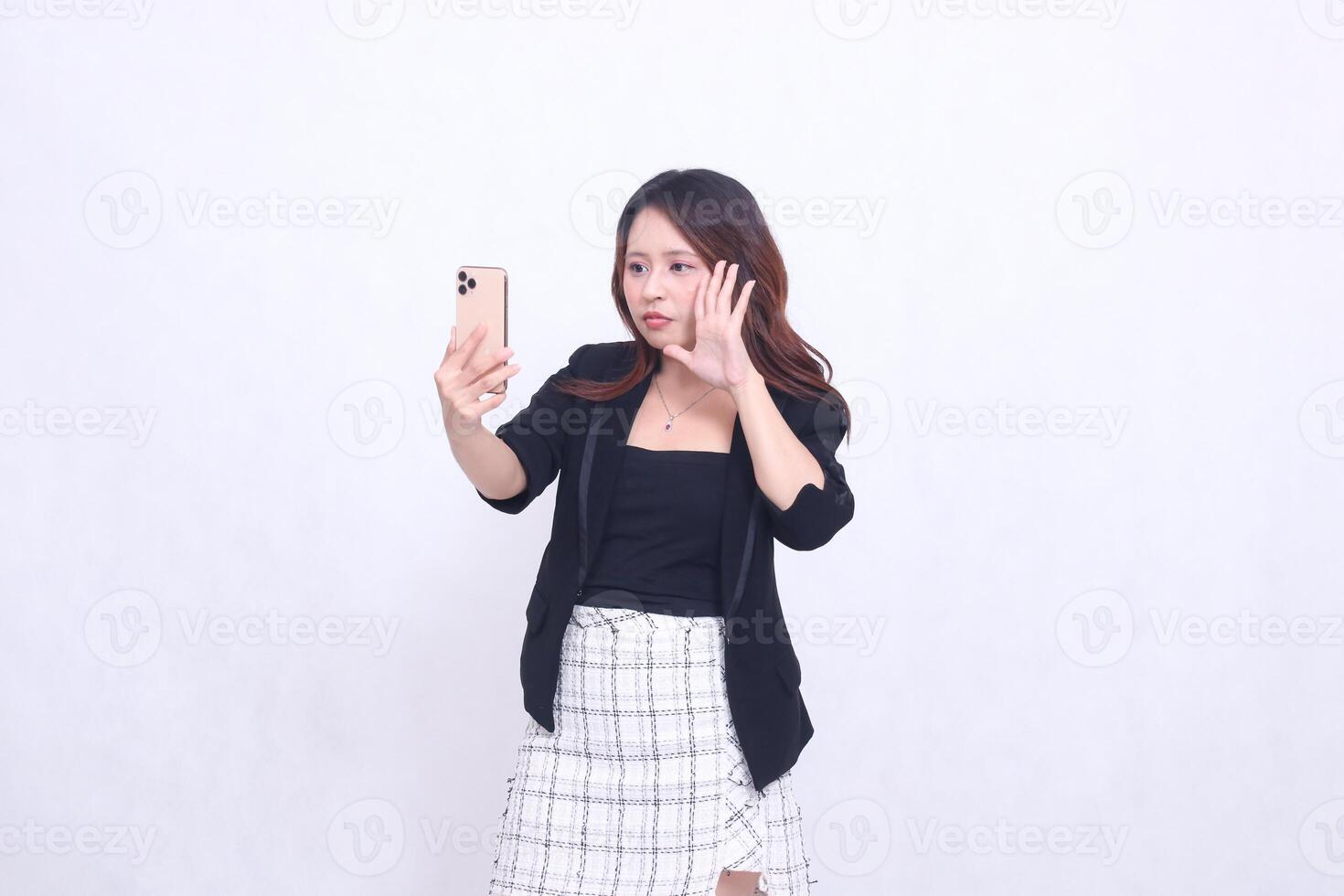 Beautiful Indonesian office woman in her 20s flat expression looking at her cream colored cellphone gadget while making a call for a promo isolated on a white background photo