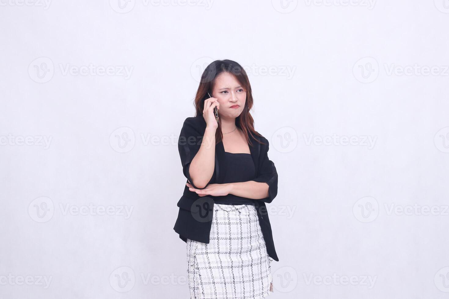 the charm of a beautiful Asian office woman in her 20s with a sullen expression while making a phone call on a cellphone gadget with her arms crossed isolated on a white background photo