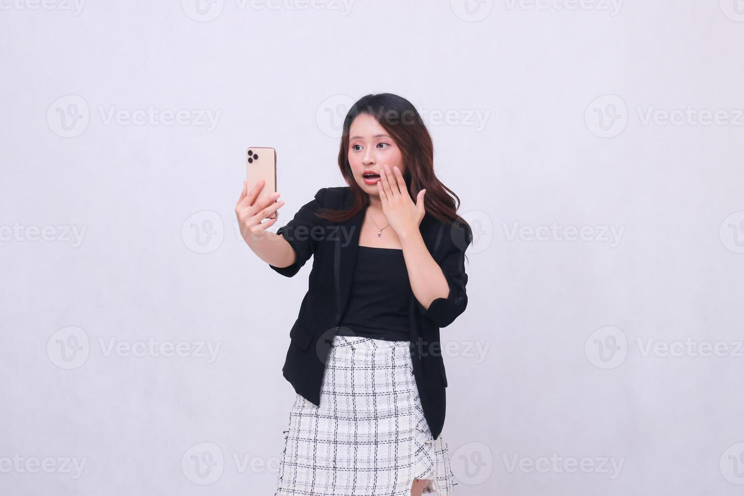 beautiful Indonesian office woman in her 20s with a shocked expression looking at her cream colored cellphone gadget while making a call for a promo isolated on a white background photo