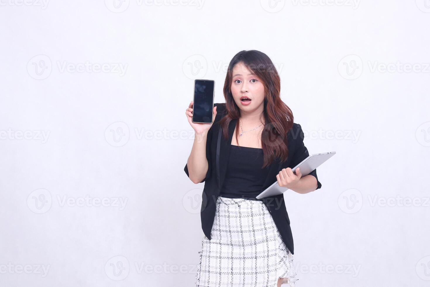 Beautiful Indonesian woman in her 20s, formal office, surprised to see a black cellphone gadget and carrying a tablet for promotion isolated on a white background photo