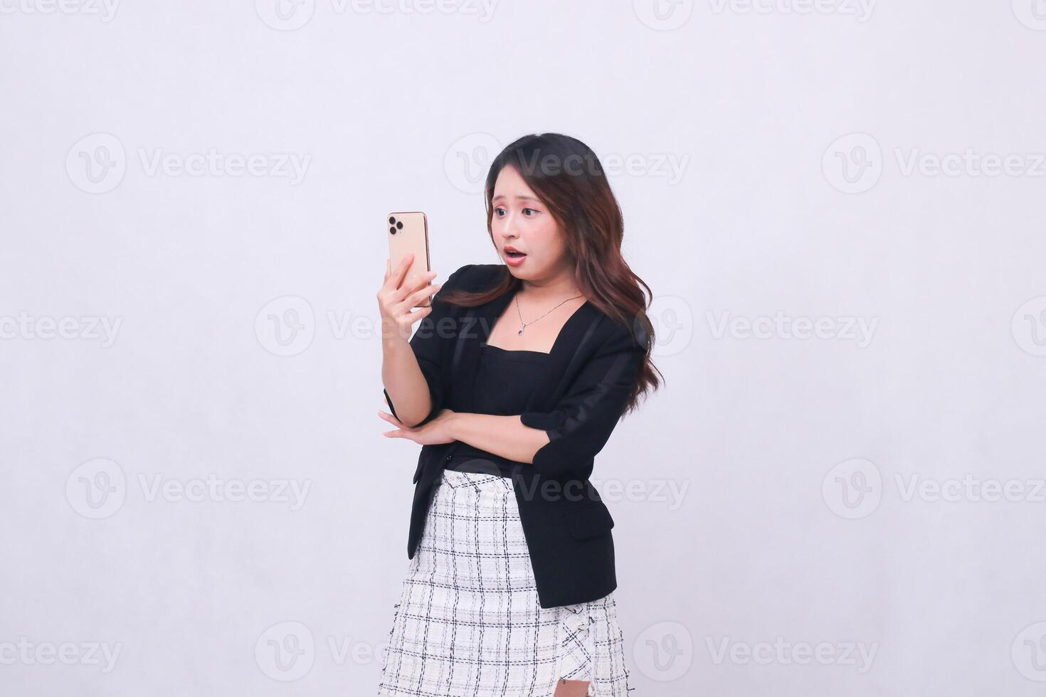 Beautiful Indonesian office woman in her 20s with a shocked expression looking at her cream colored cellphone gadget for promo isolated on a white background photo