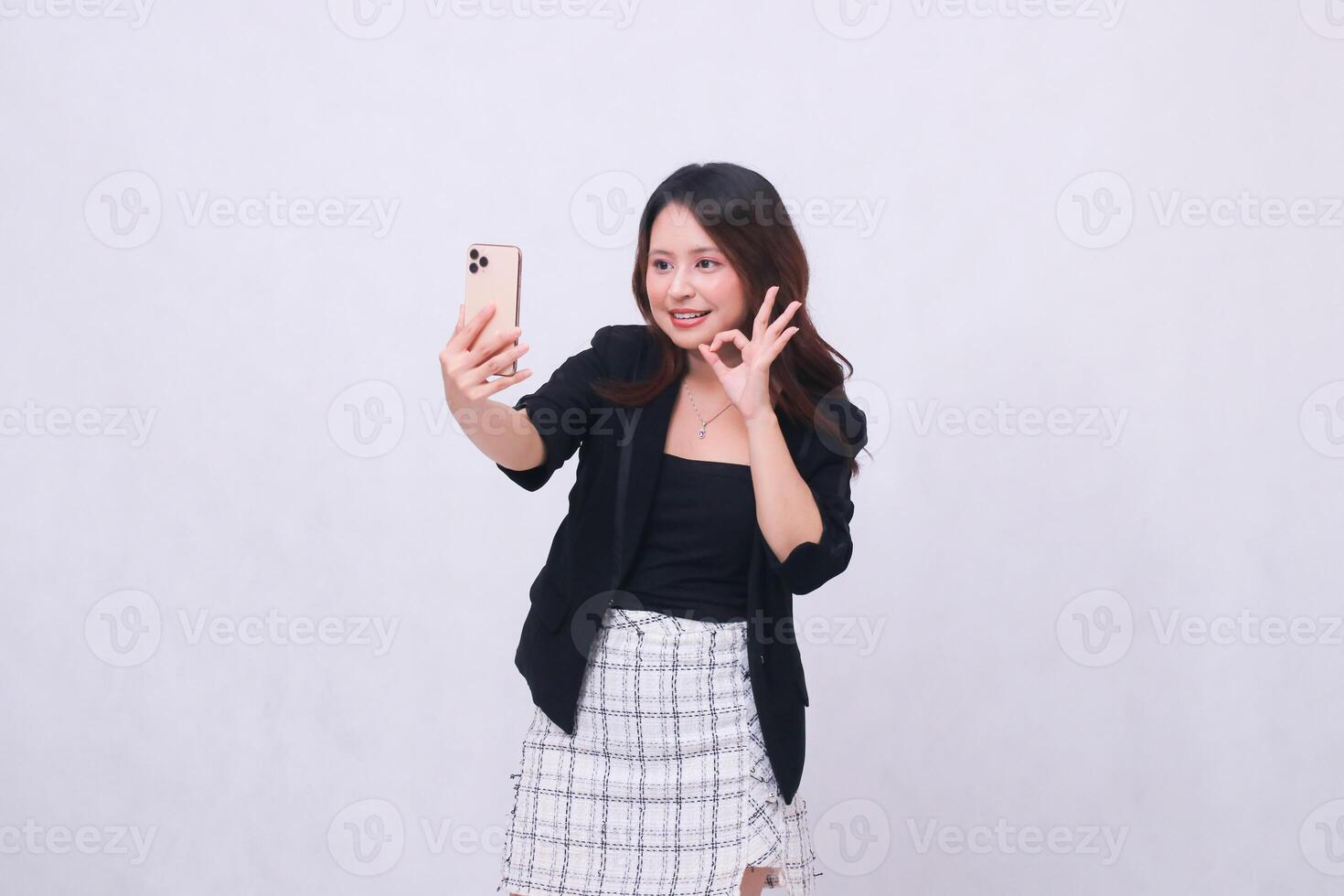 beautiful Indonesian office woman in her 20s smiling expression okay looking at her cream colored cellphone gadget while making a call for a promo isolated on a white background photo