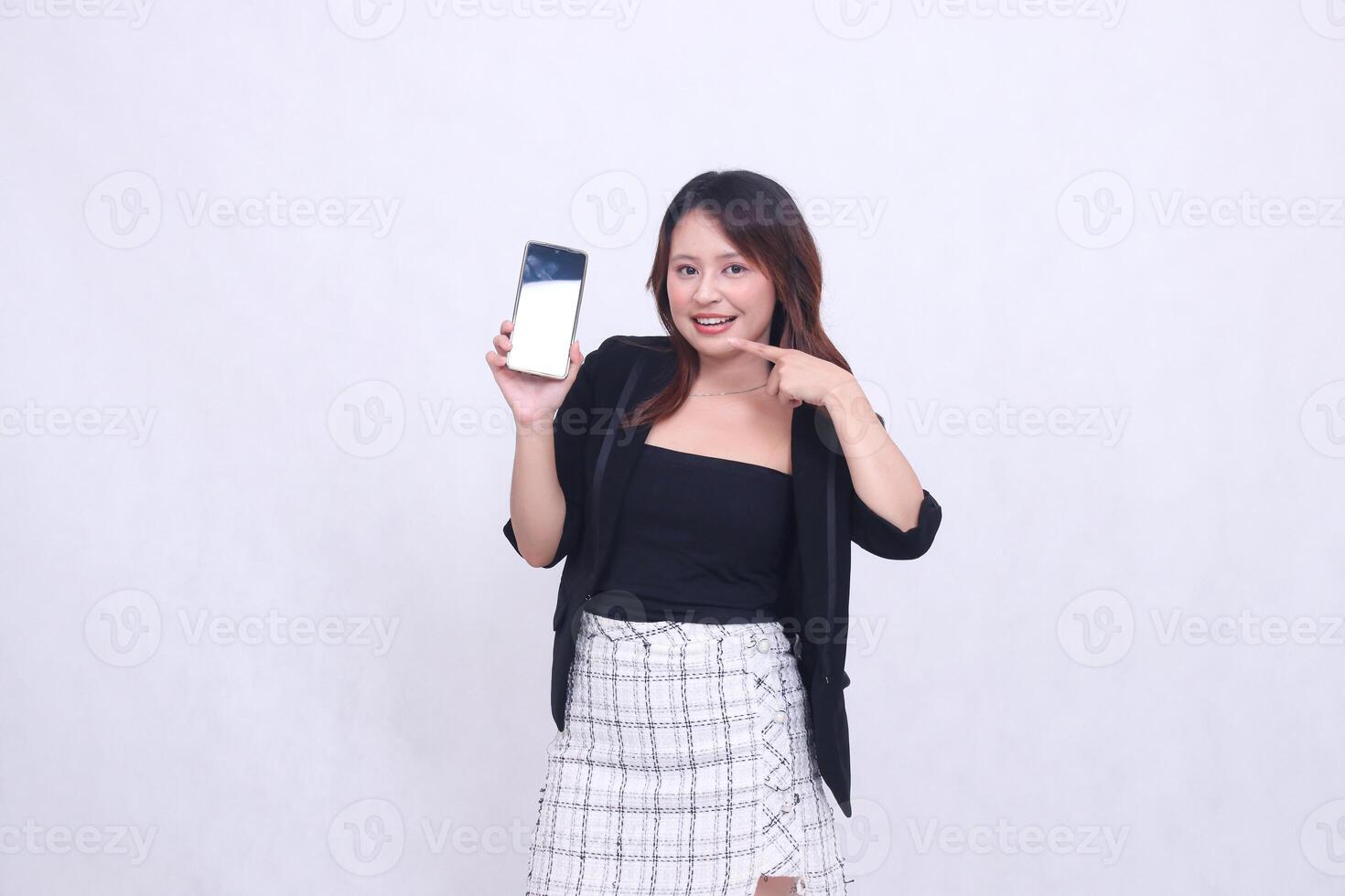 charm of beautiful Asian office woman 20s cheerful smile expression pointing right cellphone gadget for promo while arms crossed isolated white background photo
