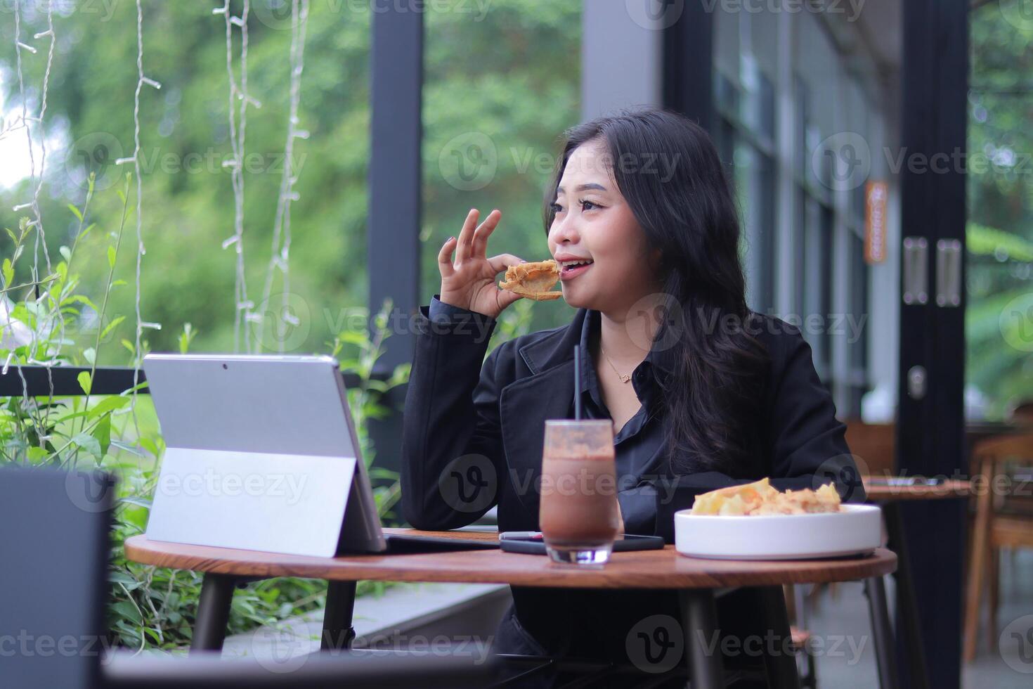 the elegance of a young Asian woman in a candid online meeting snacking in front of a laptop in a cafe photo