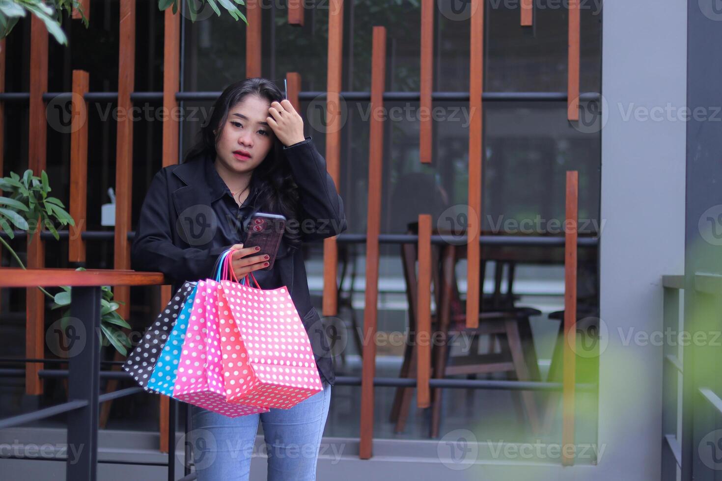 Young Indonesian office woman gracefully throws back her hair, standing against the fence carrying paperbags, credit cards and cellphones to promote online content, lifestyle, catalogs photo