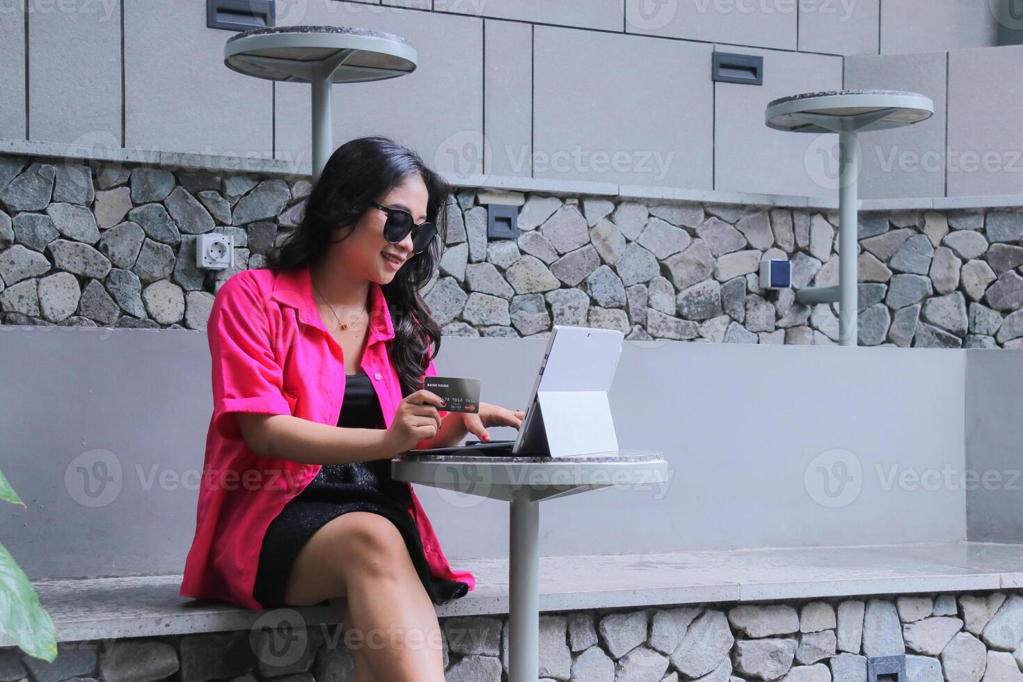 beauty of young asian woman wearing glasses smiling sitting operating laptop tablet holding credit card for promo content, fashion, business, marketing photo