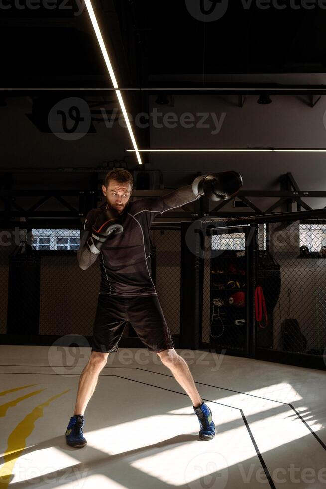 Concentrated boxer engaging in shadow boxing in empty dimly gym photo