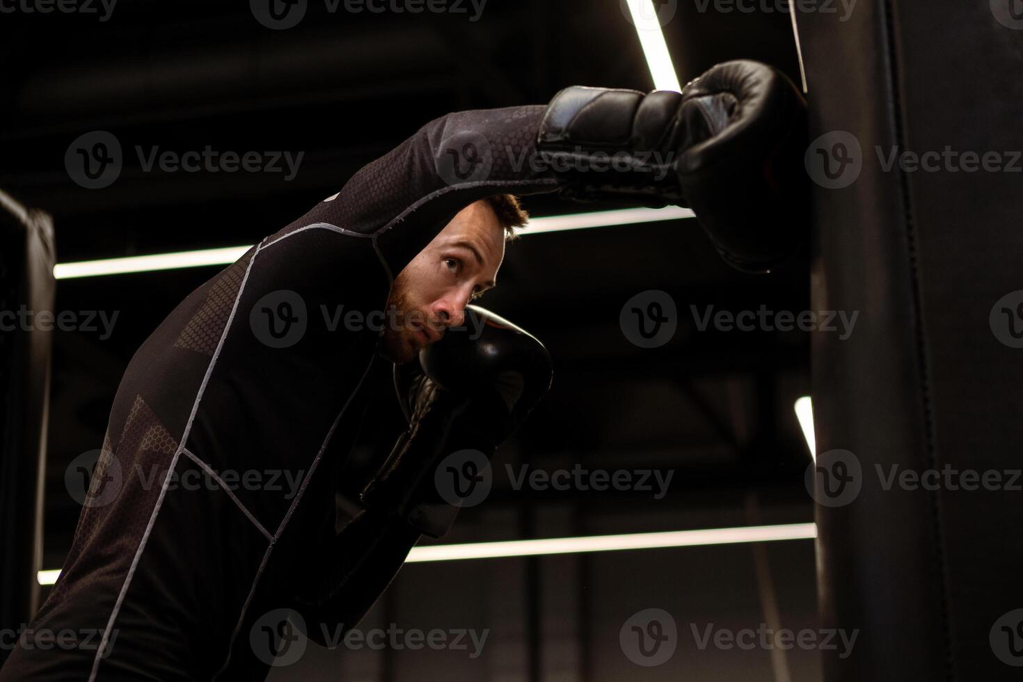 Concentrated boxer practicing punches on heavy bag in gym photo