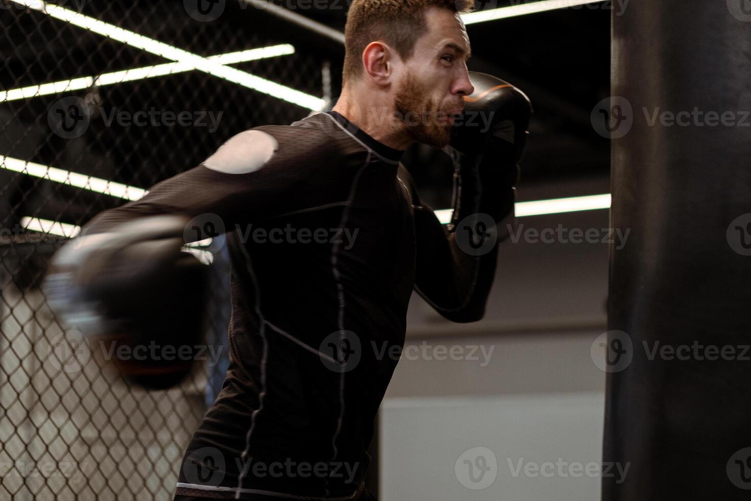 Determined boxer throwing right hook at heavy bag at gym photo