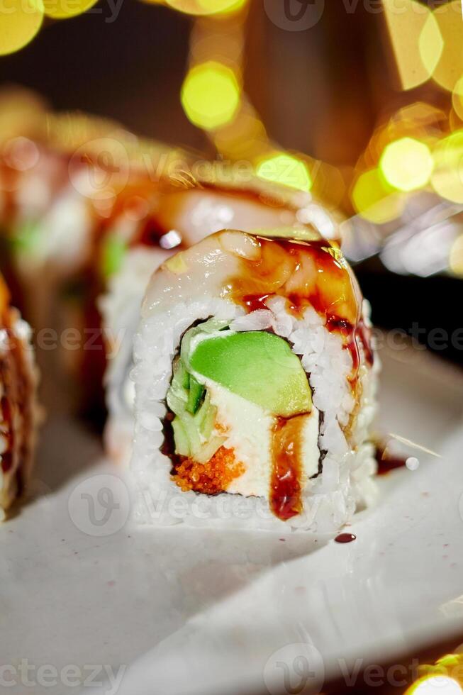 Sushi roll with scallop, cream cheese, masago and avocado against festive lights photo