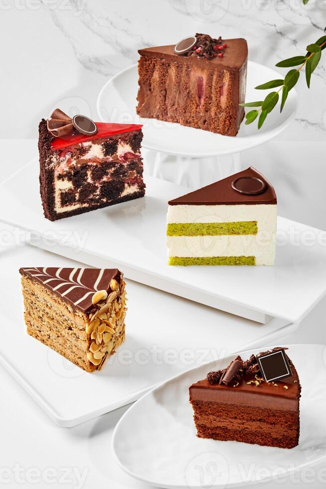 Slices of various cakes arranged on plates on marble surface photo