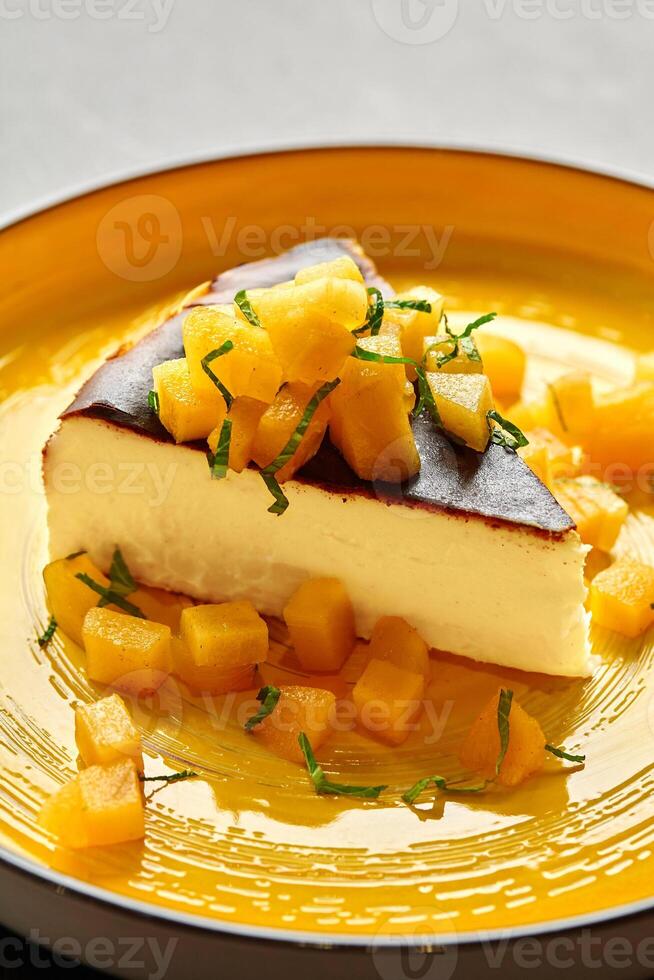 Slice of cheesecake with caramelized mango cubes and mint photo