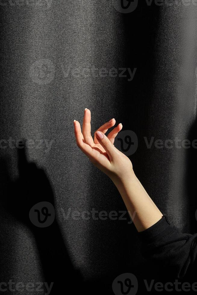 Elegant female hand poised against dark fabric with shadow photo