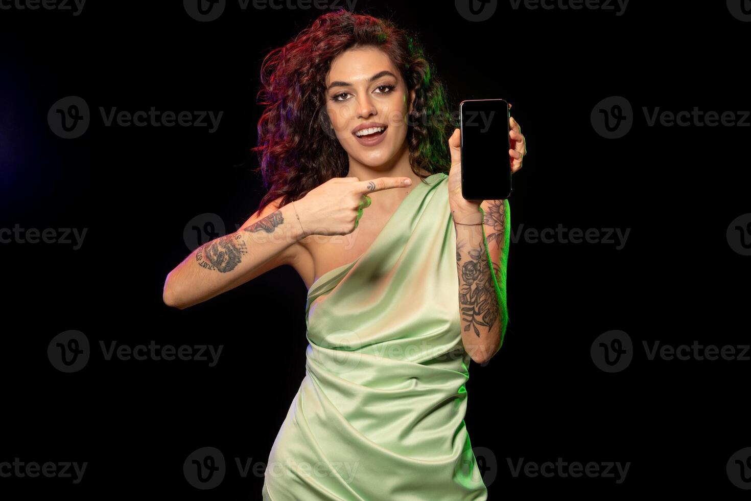 Cheerful young woman pointing at blank screen of smartphone photo